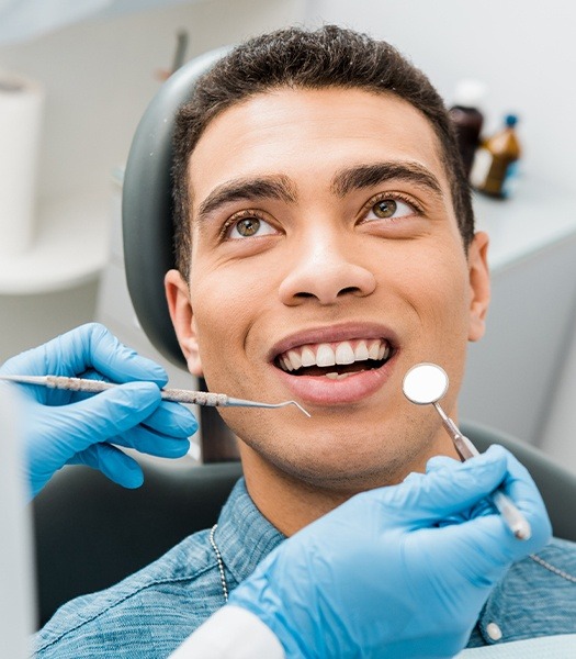 man smiling up at dentist while they hold dental tools