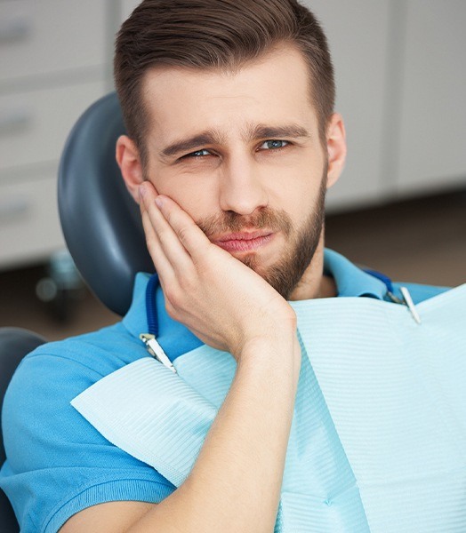 man in exam chair holding cheek in pain