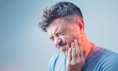 man with sever dental pain holding jaw